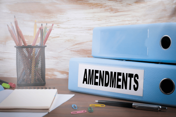 A desk with blue binders labeled "AMENDMENTS," a pencil holder, and various office supplies.